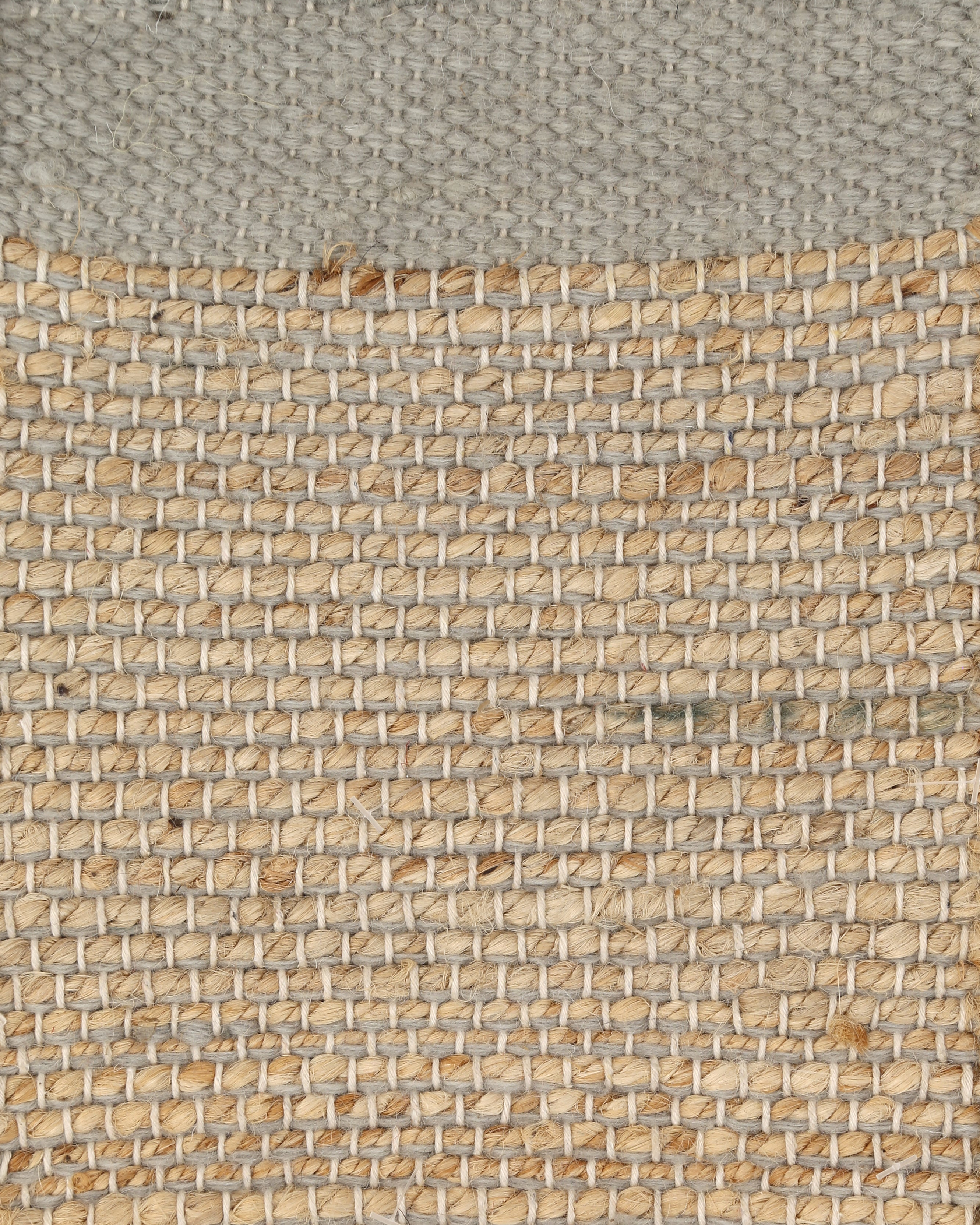 A rectangular jute rug with a solid gray border and a patterned center showcasing a mix of beige and brown tones.