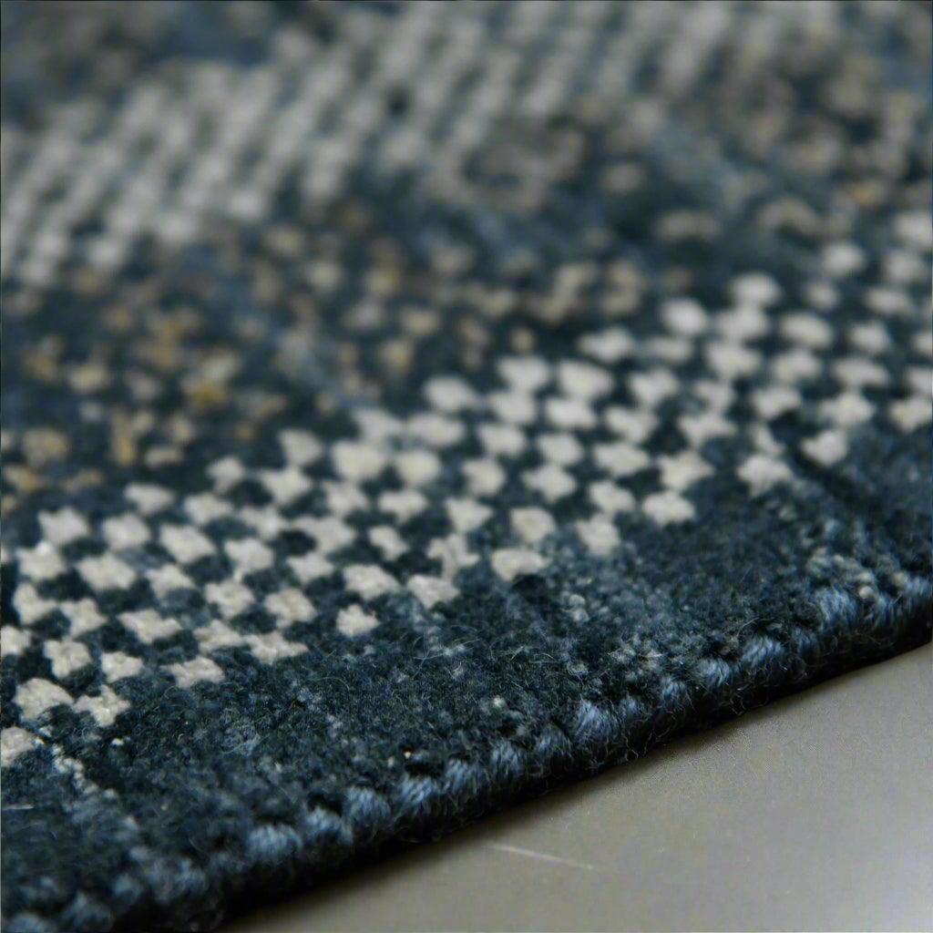 Close-up of a textured blue and gray rug corner on a concrete floor.
